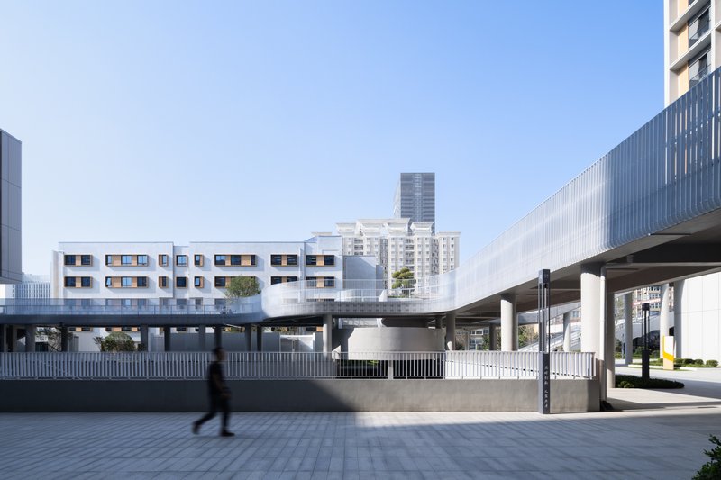 Elevated pedestrian bridge connecting white volumes with punched window openings against a backdrop of high-rise towers