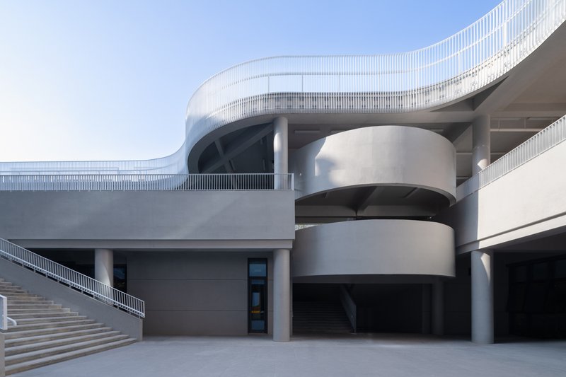 Exterior plaza showing the curved white metal facade with cylindrical volumes and an exterior staircase