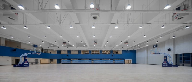 Basketball gymnasium with retractable bleachers, exposed truss ceiling and blue painted accent walls flanking the court