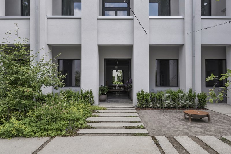 Courtyard entry with white concrete facade, deep recessed portals and planted beds flanking stone paving strips