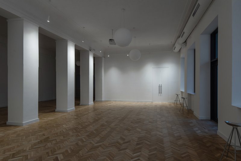 Open room with white columns framing doorways, herringbone wood flooring and sphere pendant lights overhead