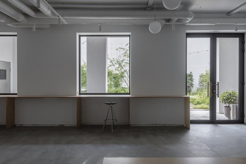 Long counter with exposed concrete base and oak top facing tall windows overlooking a planted terrace