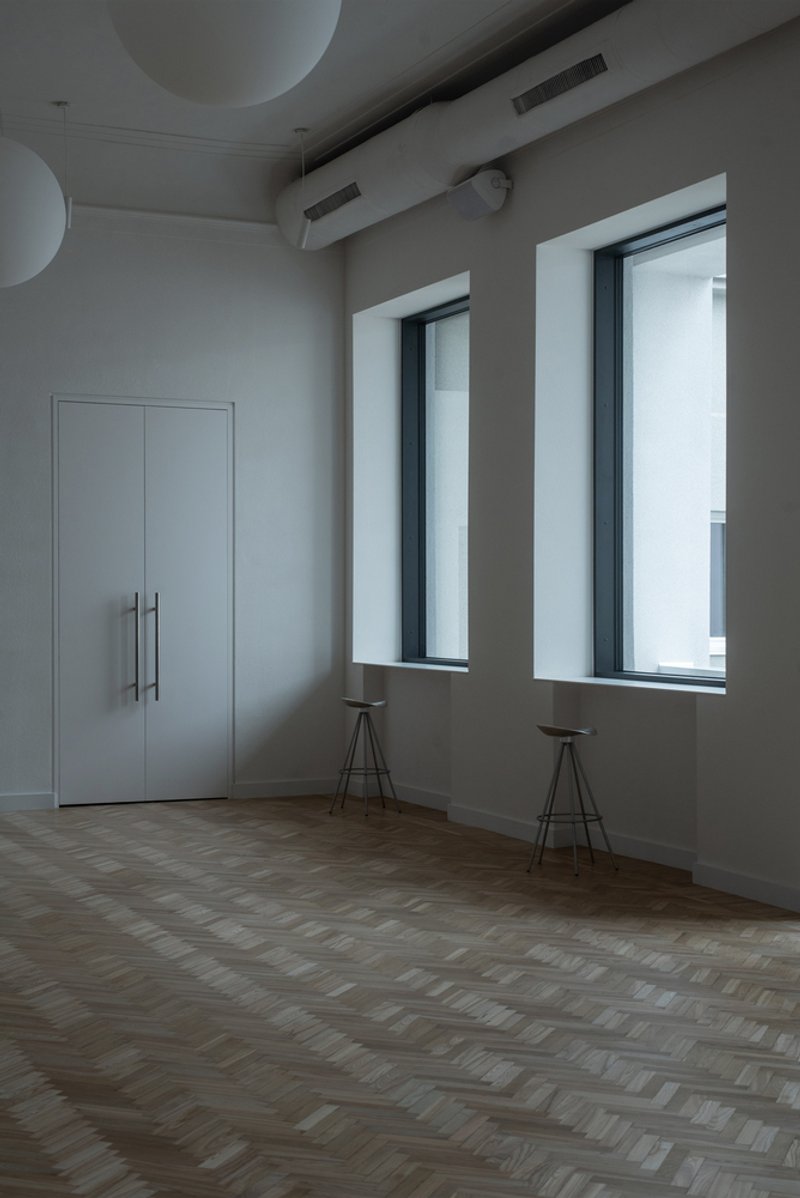 Corner room with two deep-set windows, herringbone oak flooring and two tripod stools beneath the openings