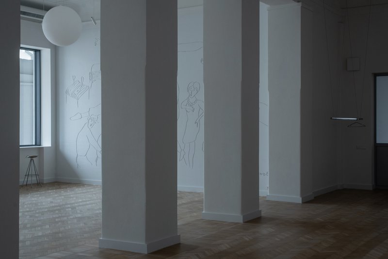 View through white columns showing parquet flooring and line drawings on the far wall