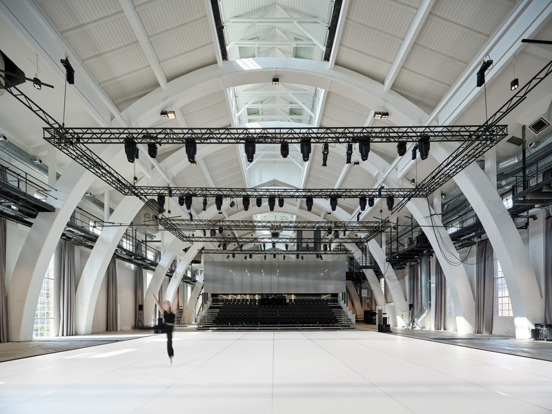 Event hall with steel truss lighting grid, white structural ribs, and pitched roof with skylights