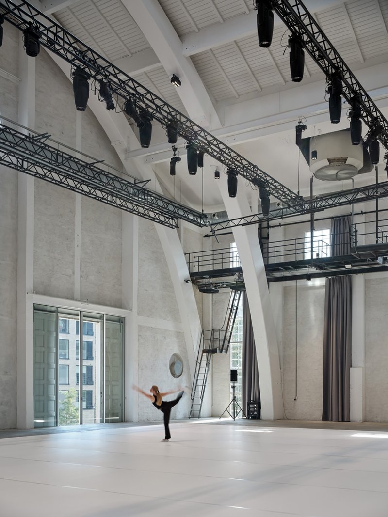 Performance space showing concrete walls, suspended lighting trusses, and a dancer stretching on the floor
