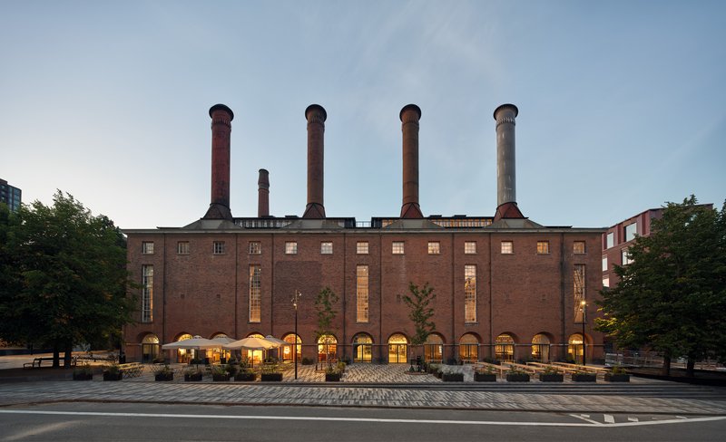 Evening view of the illuminated brick facade with five chimneys glowing against a twilight sky