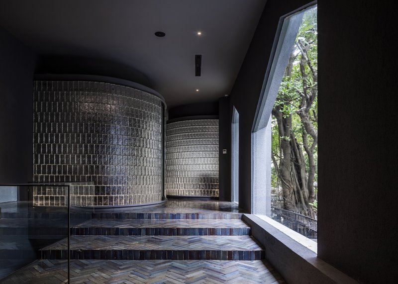 Curved patterned block walls flanking herringbone tile steps beneath a sloped black ceiling