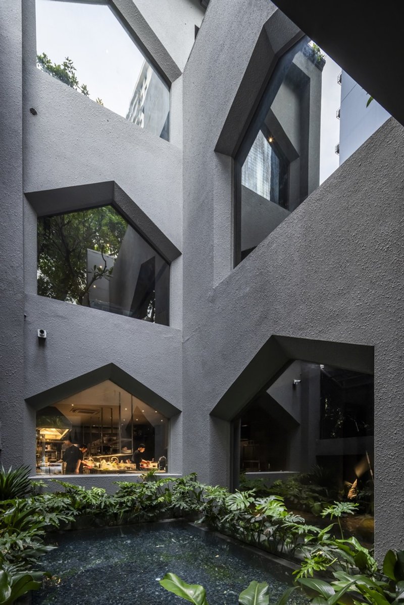 Interior courtyard with pentagonal openings revealing planted beds and a reflecting pool at dusk