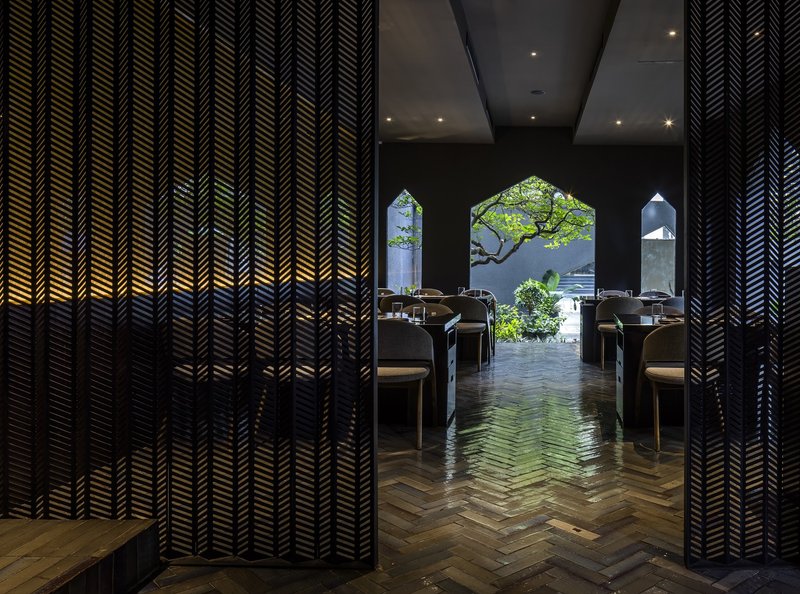 Herringbone timber floor between chevron-patterned screens framing house-shaped openings to garden