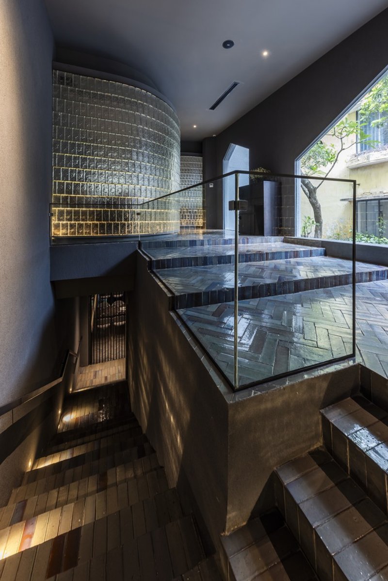 Multi-level interior with curved glass block wall and tiled staircase under glazed roof
