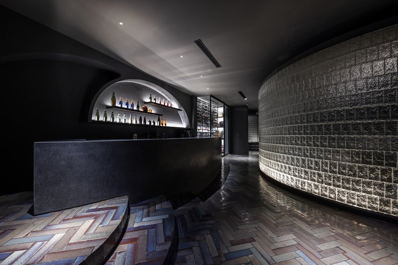Bar area with curved glass block wall, herringbone wood flooring, and arched bottle display alcove
