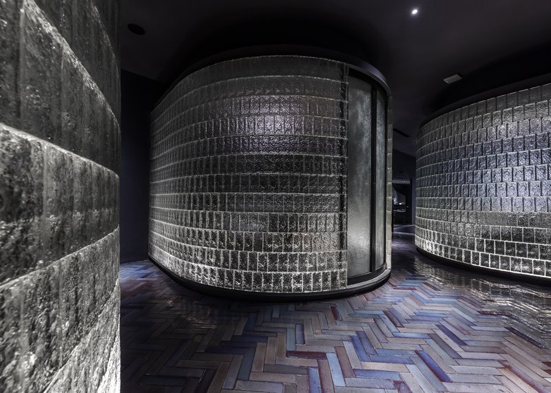 Corridor showing cylindrical glass block volume, textured concrete wall, and chevron pattern wood floor
