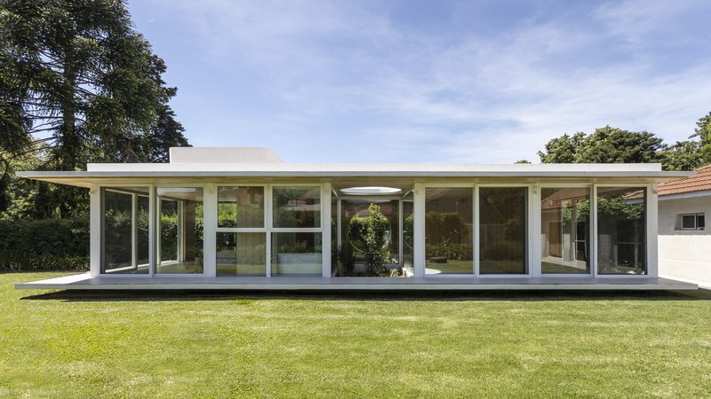 Garden facade with continuous glass walls and flat roof overhangs surrounded by lawn and mature trees