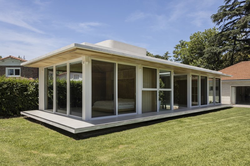 Angled view of the glazed pavilion on a raised plinth surrounded by hedges and lawn