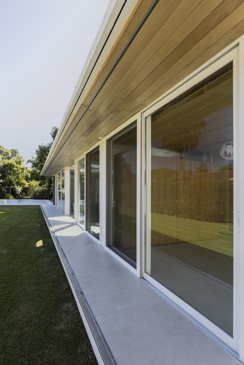 View along the concrete terrace showing the rhythm of sliding glass panels beneath the timber ceiling