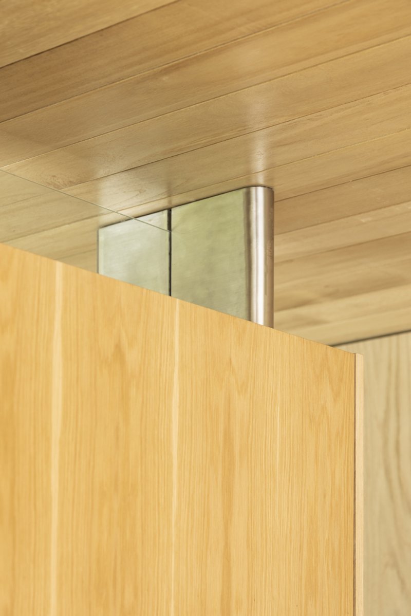 Detail of a cylindrical steel hinge connecting wood panels beneath a timber ceiling