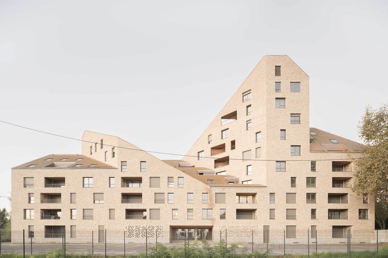 Pale brick residential complex with stepped gabled forms and recessed balconies under an overcast sky