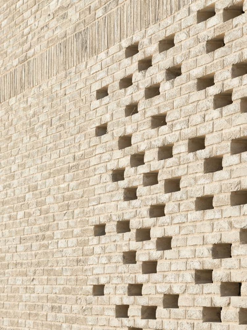 Close-up of pale brick wall with scattered square perforations casting shadows in sunlight