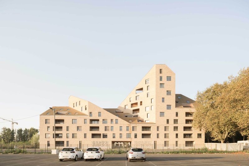 Stepped massing of pale brick volumes rising against a clear evening sky with parked cars below