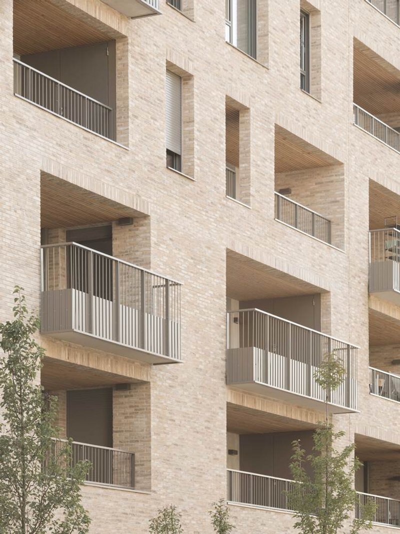 Staggered balconies with timber soffits and metal railings set into a pale brick facade with young trees