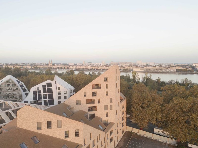 Aerial view of clustered gabled volumes overlooking the river and city skyline at dusk