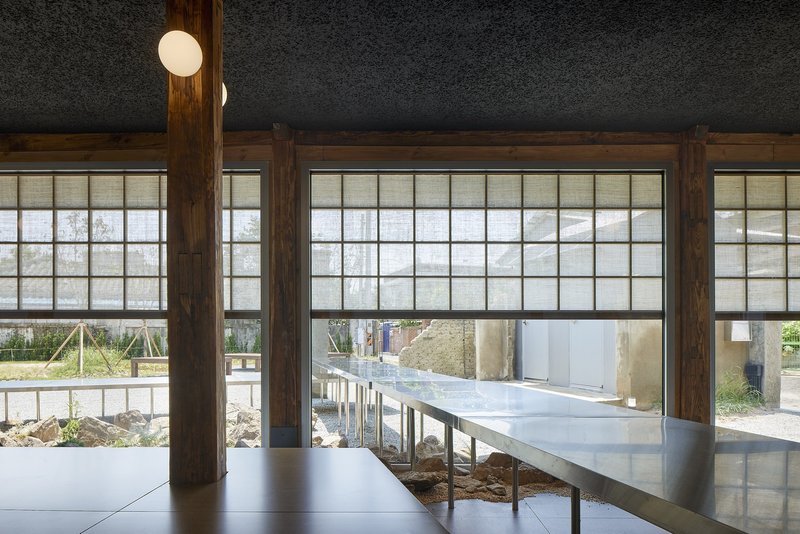 Interior view through timber-framed shoji screens with elevated steel table bridging exposed earth beneath