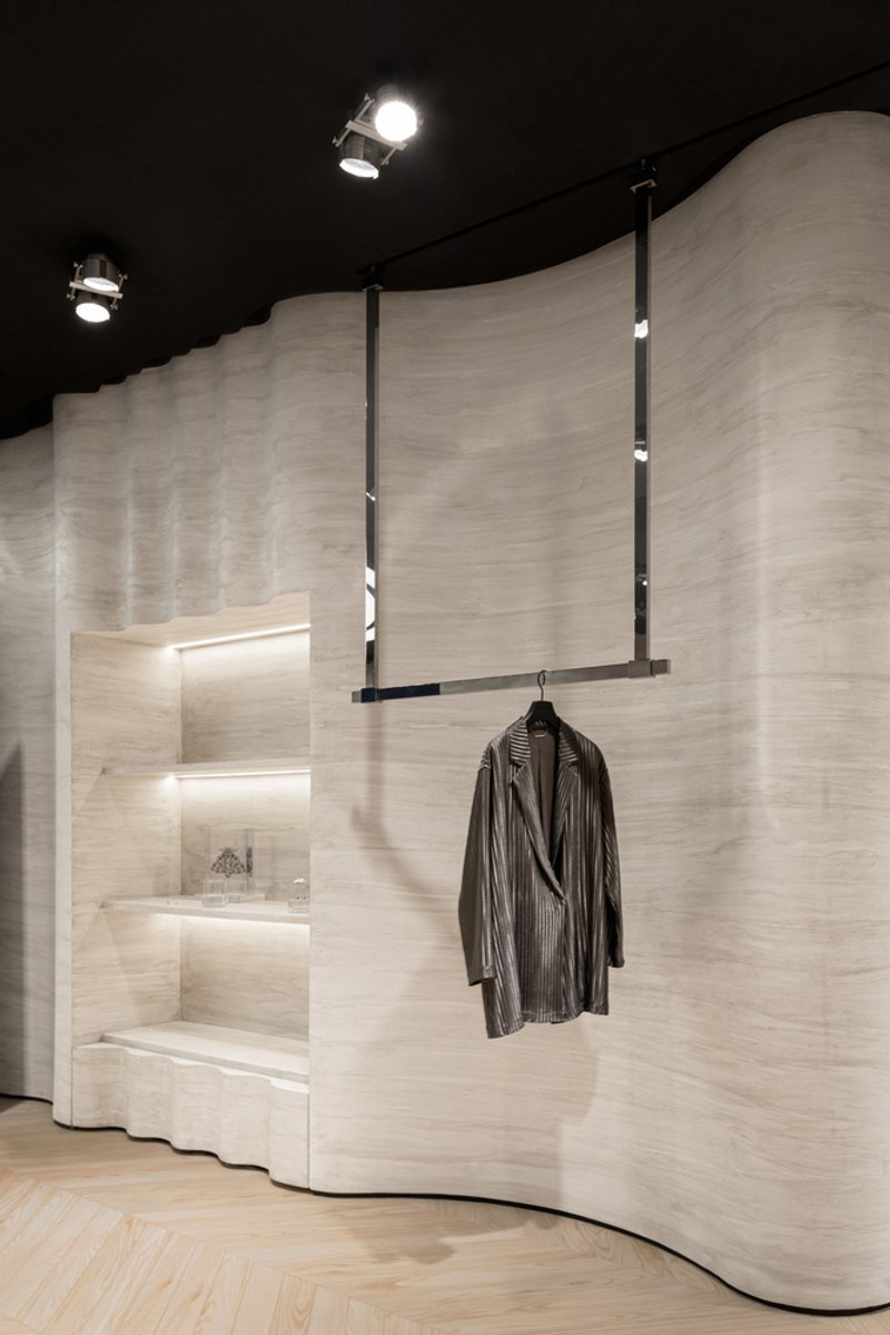 Close-up of undulating pale wood wall with integrated display niches and suspended metal clothing rail