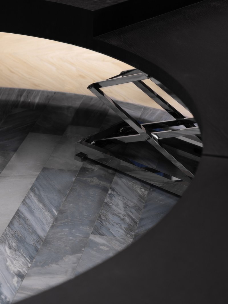 Angled glass balustrade reflecting striped marble floor beneath a curved black ceiling plane