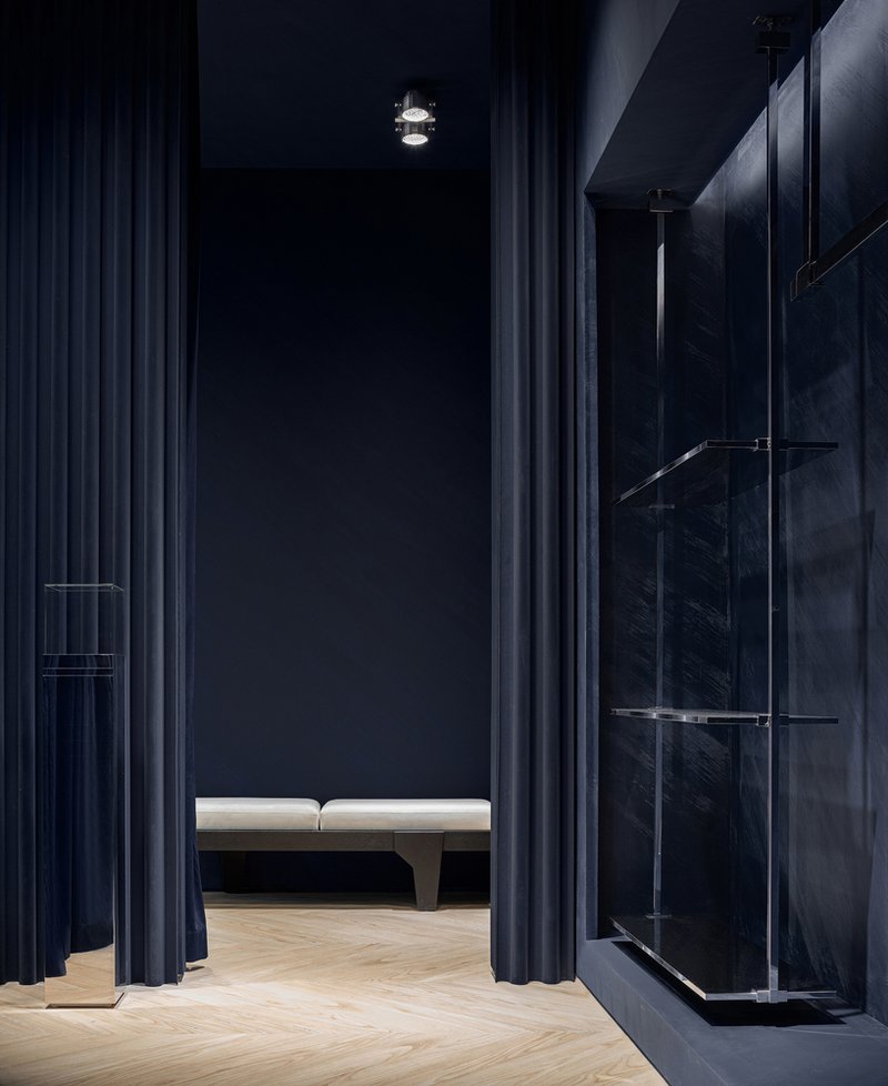 Retail interior hallway with floor-to-ceiling blue curtains and glass display shelving along marble wall