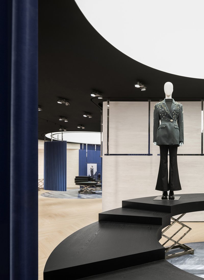 Retail interior with black curved ceiling and elevated platform displaying a mannequin under recessed spotlights