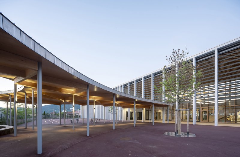 Covered courtyard with white columns supporting a timber soffit at dusk with interior lights glowing