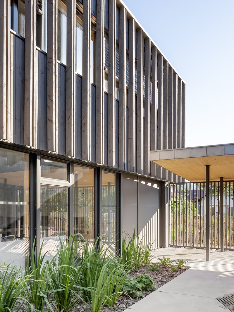 Exterior facade with vertical metal louvers above planted beds and timber pergola structure