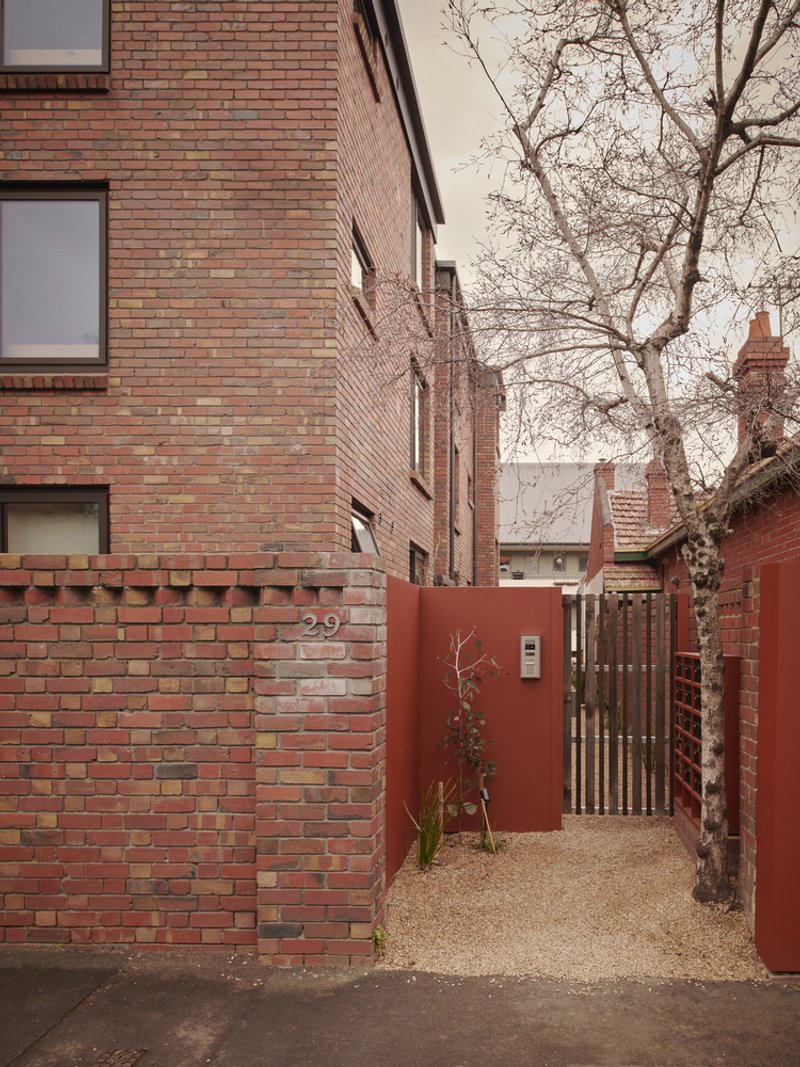 Brick entry courtyard with red metal gate and bare winter tree