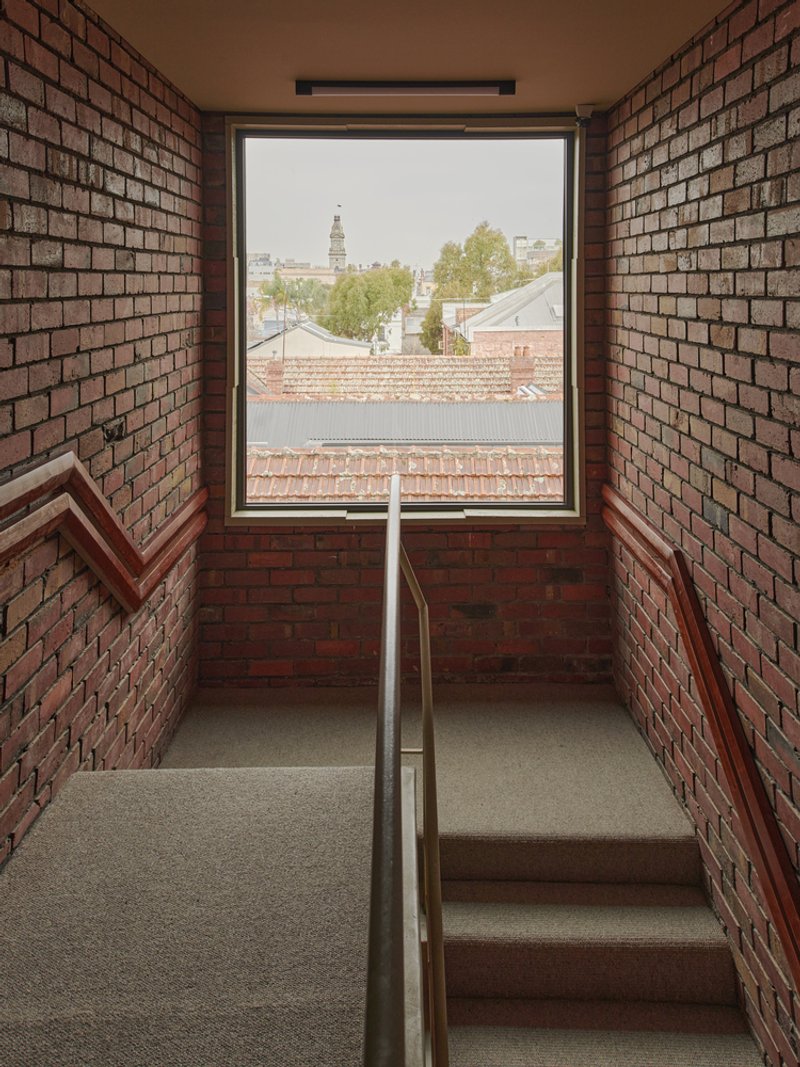 Stairwell landing with exposed brick walls framing a window onto rooftops