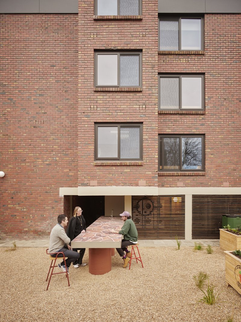 Courtyard table with four people gathered beneath a multicolored brick facade