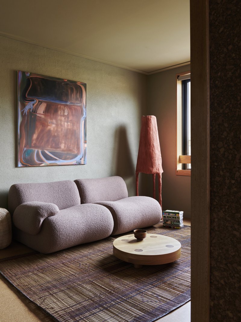 Living room with textured sofa and conical lamp in afternoon sunlight filtered through a narrow window