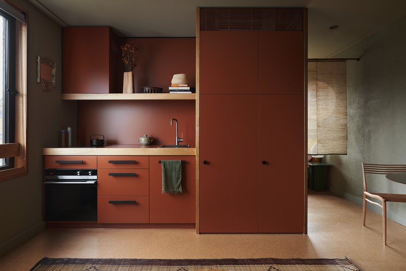 Kitchenette with terracotta-toned cabinetry and open shelving beneath cork flooring