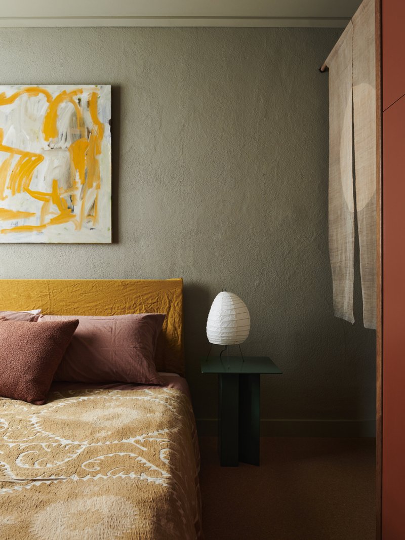 Bedroom corner with sage green walls, timber sliding door jamb and dark glass bedside table with white lamp