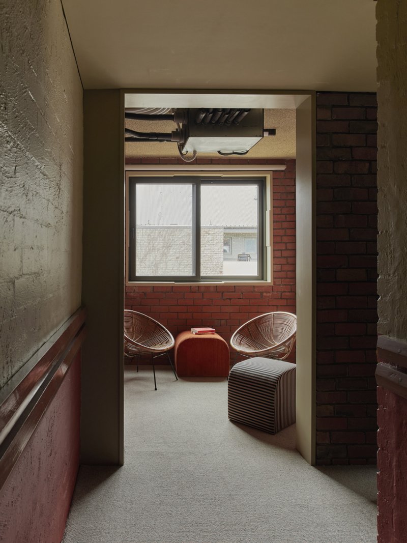 View through doorway to seating nook with wire chairs and red brick window wall under overcast light