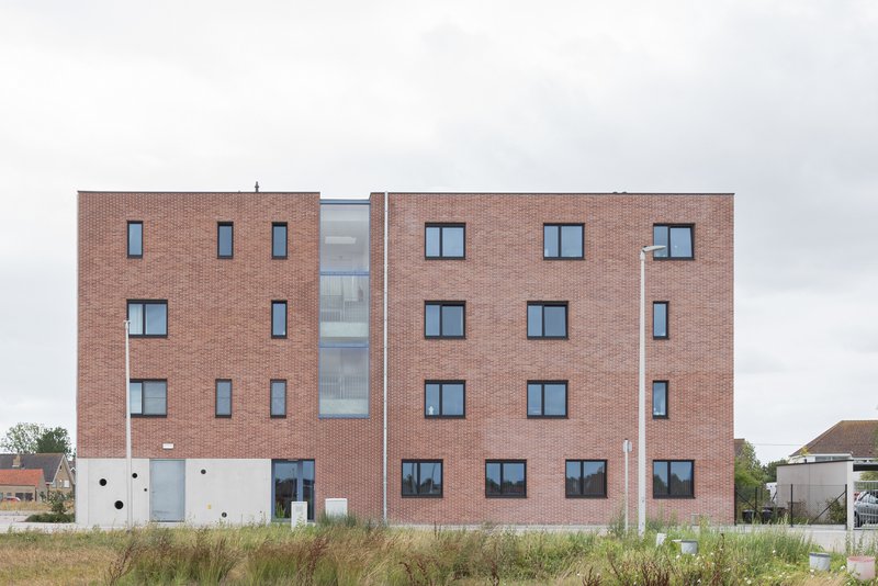 Rear elevation showing red brick volumes flanking a central glazed circulation core under overcast sky