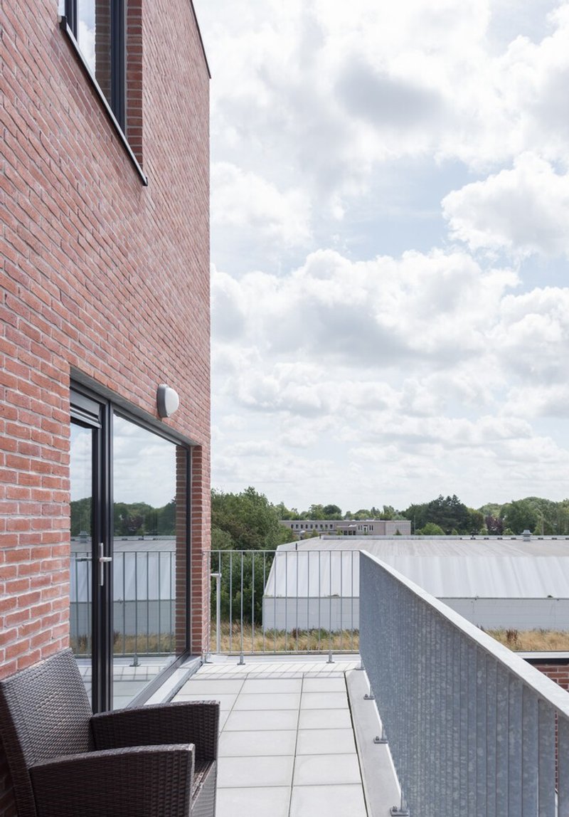Private terrace with light grey pavers and metal railing looking toward neighboring rooftops under cloudy sky