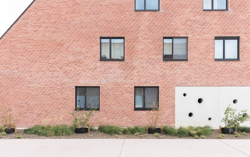 Red brick facade with rectangular windows and white panel punctured by circular openings at ground level
