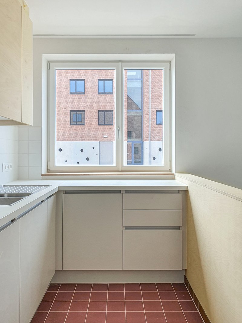 Kitchen window framing view of the brick courtyard facade with light wood cabinetry and terracotta floor