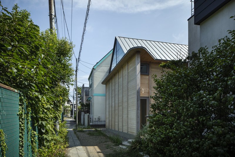 Street view of the timber-clad facade with curved gable and standing seam metal roof between neighboring buildings