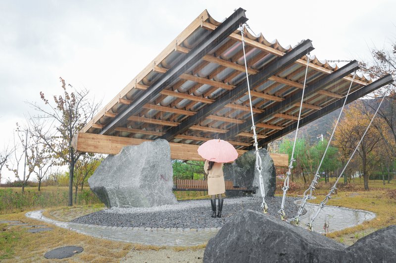 Exposed timber roof structure with cable suspension and a visitor holding a pink umbrella beneath