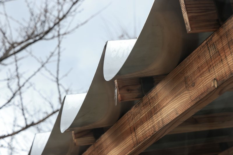 Close-up of curved roof tiles resting on timber beams against bare winter branches