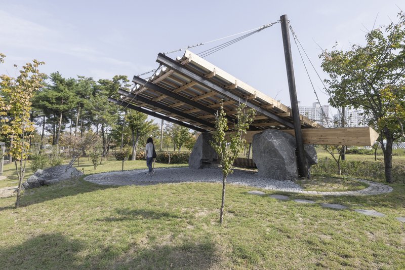 Side view of the cable-suspended pavilion with gravel ground surface and surrounding trees in autumn
