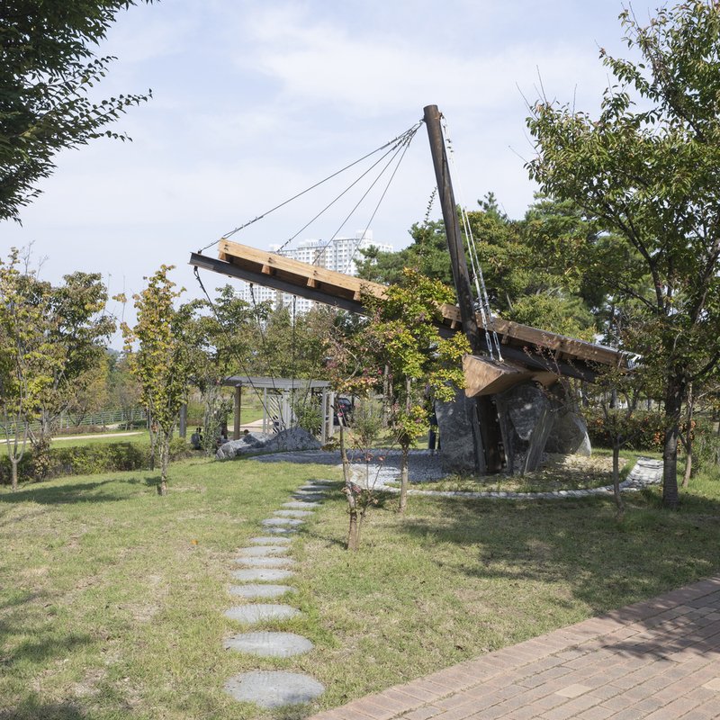 Tensioned timber roof structure anchored to a standing stone beside stepping stone path