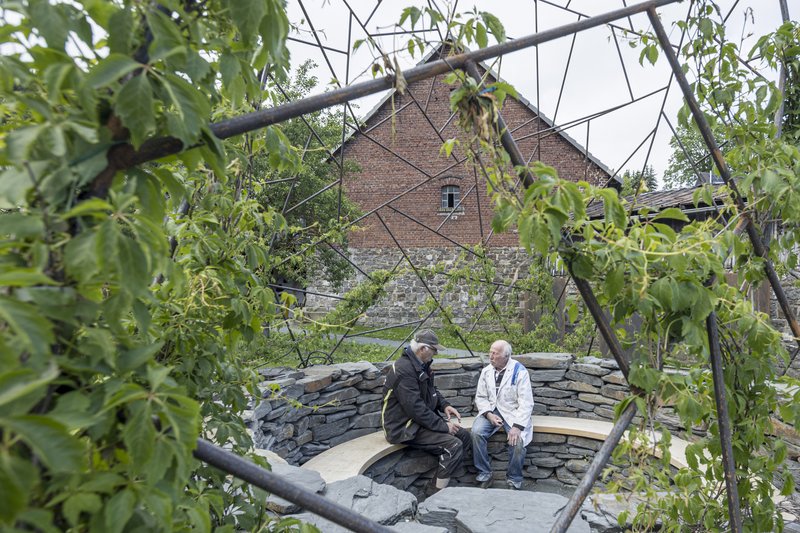Two visitors seated in the slate-walled enclosure beneath the triangulated steel lattice and fruit tree branches